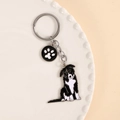 Detail eines Border Collie Schlüsselanhängers aus Metall mit Hundemotiv auf weißem Teller - Sitzender Border Collie