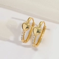 Detalle de pendientes de aro dorados con corazón y circonitas sobre fondo de seda blanca - Corazón
