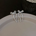 Detalle de pendientes de lazo plateados con circonitas brillantes sobre bandeja gris - Plateado