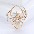 Detailed view of a gold spider brooch with a large faceted clear gemstone on a white base - Spider / Gold