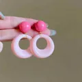 Vue détaillée des boucles d'oreilles en acrylique rose avec détails dorés en main - Boucles d'oreilles géométriques boule et anneau roses