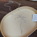 Detail view of silver bow necklace with teardrop pendants on a beige tray - Bowknot Water Drop Tassel Necklace / Silver