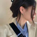 Minimalistische hartvormige zilveren oorringen gedragen door een model in elegante kleding - Witgoud
