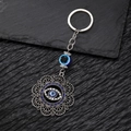 Detailed view of silver evil eye and hollow hamsa hand keychain on dark stone - Flower Blue Eye