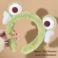 Close-up of a green plush frog headband with white wings and big eyes for skincare - Hair Hoop-Big Eyes