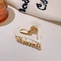 White acetate heart hair claw clip with gold metal teeth on beige knit background - White