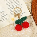 Handmade woven cherry keychain with red fruit, green leaves, and white flower on gold ring - Cherry