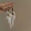 Bohemian long white feather earrings with golden leaf charms shown on a hand - White Feather Leaf Style (49#)