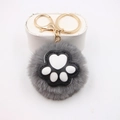 Close-up of grey plush cat paw pompom keychain with white pads and gold metal ring - Cat Claw Gold Keychain / Gray