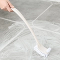 Beige long-handled toilet brush with white bristles cleaning foamy bathroom floor tiles - Beige