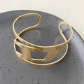 Top view of a gold wide cuff bracelet with geometric hollow cuts on a grey ceramic plate - Hollow Geometric Bangle / Gold