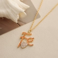 Macro detail of gold Fe letter pendant necklace with orange enamel and crystal heart charm - Orange