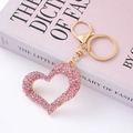 Detailed close-up of a pink crystal heart keychain with a golden lobster clasp on a book - Gold Hollow Pink Rhinestone Heart