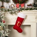 Calza di Natale in velluto rosso con lettera C dorata davanti a un camino addobbato - Lettera C