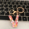 Letter V resin keychain with colorful heart sequins and gold ring on a laptop keyboard - Letter V