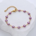 Detalle de pulsera ojo turco dorada con abalorios morados sobre piedra blanca y cierre mosquetón - Morado