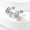 Detailed view of silver triple-ridged C-shaped hoop earrings on a white display - Silver