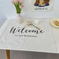 Minimalist beige linen table mat with 'Welcome TO OUR BEGINNING' black artistic lettering - 50x68cm / White