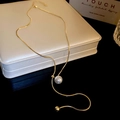 Detalle de un collar de cadena de serpiente dorada con perla blanca en un joyero - Dorado