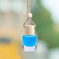 Car fragrance pendant with blue liquid, wooden cap and woven rope in nature setting - Sky Blue Ocean Scent