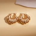 Dettaglio macro di orecchini a cerchio dorati con texture a conchiglia e marchio 18K - Oro