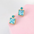 Dettaglio di orecchini geometrici in cristallo blu con base dorata su supporto rosa - Acqua