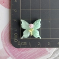 Macro shot of 3cm mint green resin butterfly accessory with pink rose on a cutting mat - Green Butterfly + Pink Rose