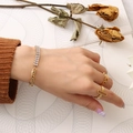 Bracciale in titanio dorato con zirconi e anelli coordinati indossati sulla mano - Bracciale Oro