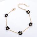 Detail van gouden armband met vijf zwarte kristallen bloemen en een stevige karabijnsluiting - Oorhaken met ketting (paar) / Zwart