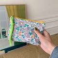 Detail einer floralen Kosmetiktasche mit gelbem Reißverschluss und neongrüner Kordel - Violettes Blumenmuster