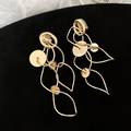 Detailaufnahme langer goldener geometrischer Fransenohrringe mit polierten Metallringen - Clip-Ohrringe / Gold