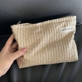 Retro beige woven clutch bag with a branded label shown held against a dark surface - Champagne Twist