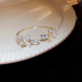 Vue détaillée du bracelet jonc feuilles en cristal sur un plateau en céramique crème - Blanc