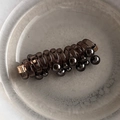 Macro detail of dark brown spiral hair coil with metallic beads on a ceramic plate - Black Spiral Pearl Style / Black Pearl Hair Braider