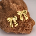 Macro shot of polished gold bow-shaped stud earrings placed on a natural textured stone - EH141-Bow Knot