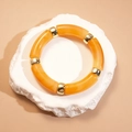 Détail du bracelet en perles acryliques ambrées avec intercalaires dorés sur support roche - Forme de Nœud de Bambou / Café Clair