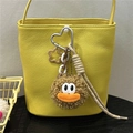 Dettaglio di un ciondolo di peluche marrone con occhi grandi su una borsa a secchiello gialla - Cachi