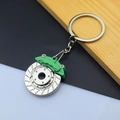 Detail of silver brake disc keychain with green caliper on wooden background - Brake Disc / Green