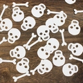 White skull and bone confetti sequins for Halloween party decoration on wooden background - White Bone + White Skull