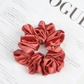 Rust red satin fabric scrunchie with silk texture and pleated design on magazine - Orange
