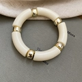 Dettaglio di perline geometriche in acrilico crema con sfere dorate su un bracciale - Bianco