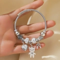 Silbernes Kabelarmband mit Teddybär-, Herz- und Schleifenanhängern am Handgelenk getragen - Silber