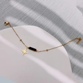 Goldenes Armband mit achtzackigem Sternanhänger und schwarzer Perle auf Tablett - Achtzackiger Stern