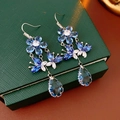 Vue détaillée des boucles d'oreilles en cristal bleu avec fleurs et papillons argentés - Bleu