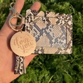 Close-up of snakeskin pattern card holder with tassel, gold hardware, and wooden charm - Brown Snakeskin