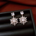 Detail of 14k gold plated snowflake earrings with zircons on dark leather and silk background - Gold