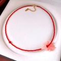 Detalle de collar de cuentas rojas con colgante de flor rosa en forro de joyería blanco - Dorado-Rojo
