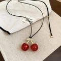 Primer plano del collar con colgante de cereza roja y hojas doradas sobre lino - Rojo