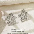 Detailed view of silver flower-shaped stainless steel stud earrings on textured surface - 3D Flower