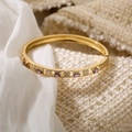 Detalle de brazalete chapado en oro 18K con piedras púrpuras y tréboles sobre tela de tweed - Dorado-Púrpura